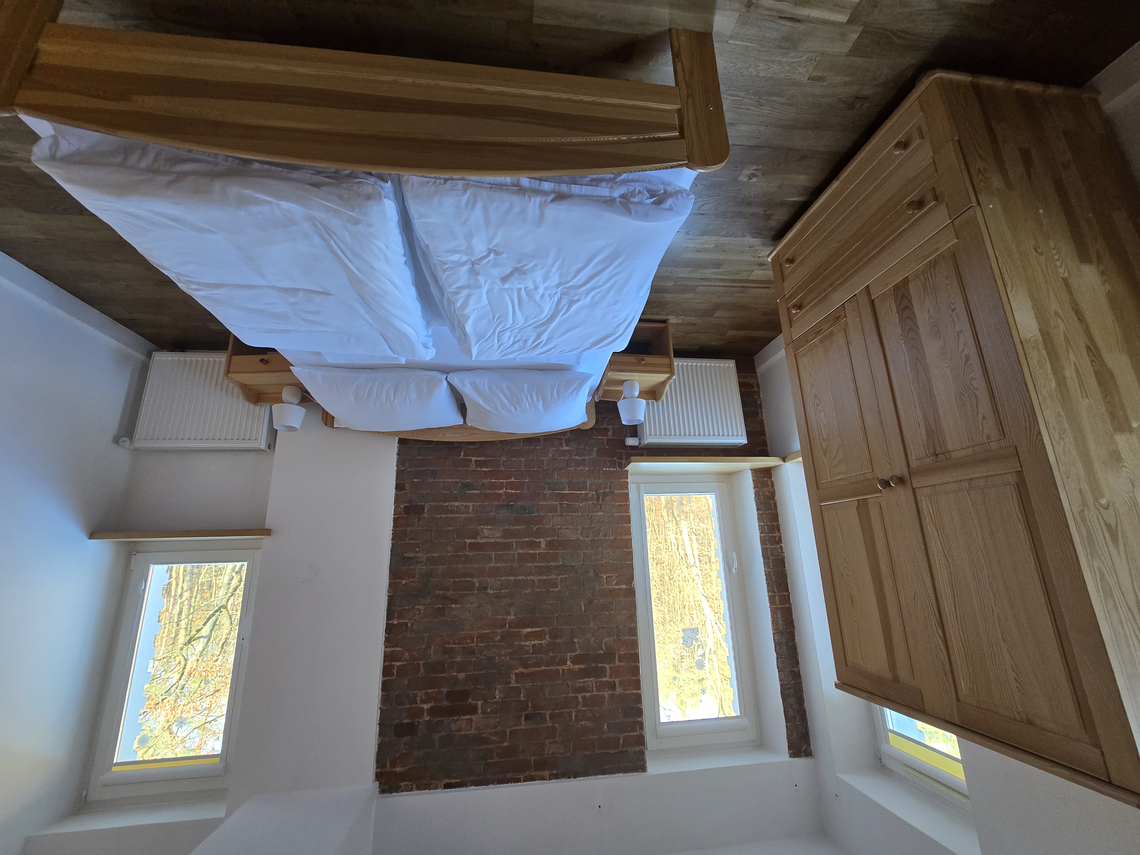 Przytulny pokój z wygodnym dwuosobowym łóżkiem oraz dużą, pojemną szafą z widocznymi barwnymi drzewami za oknem